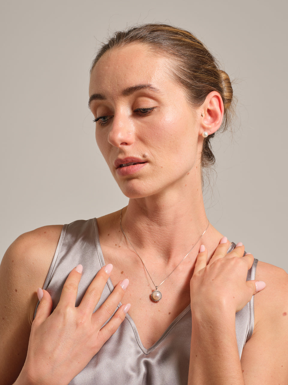 Woman wearing a silver tank top and pearl necklace against a neutral background